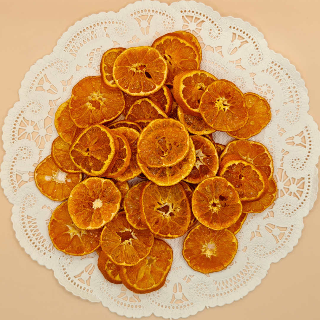 Top-down view of vibrant slow-dried mandarin chips artfully arranged on a white doily plate against a peach background