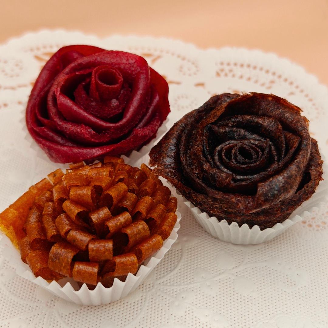 Three flower-shaped fruit leather in red, brown, and orange on a white doily.