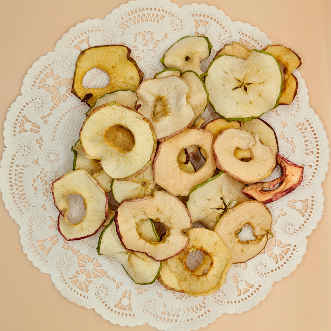 Top-down view of slow-dried apple chips piled on a white paper doily against a cream backdrop.