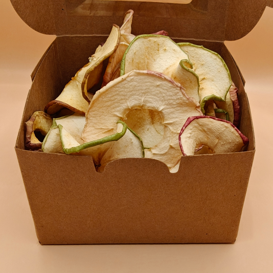 Open kraft box filled with slow-dried apple chips on a cream background