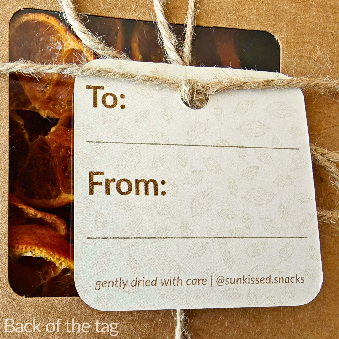 Back of the gift tag showing blank “To:” and “From:” fields and “@sunkissed.snacks” handle, tied to the box with natural twine